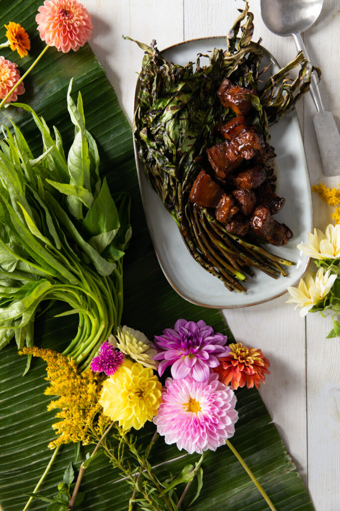 A plate of grilled water spinach and pork adobo garnished with fresh flowers and greens.