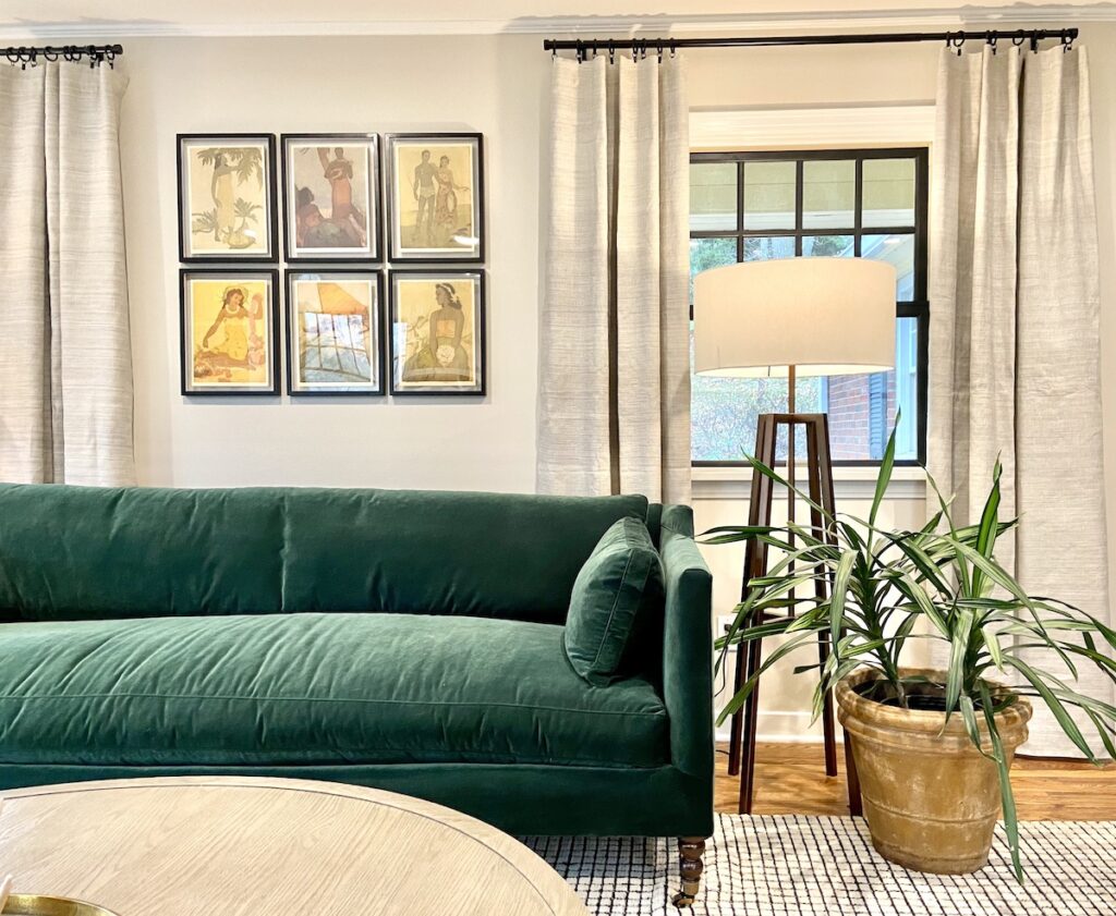 A velvet green couch against a wall with six frames on the wall