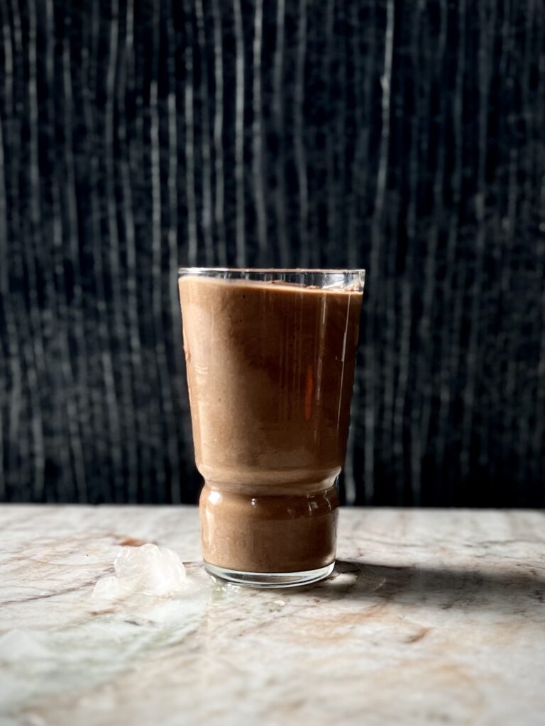 A look in of a single glass with a thick chocolate Ken-ergy: The Ultimate Post-workout smoothie and a little melting ice on the left side