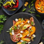 a colorful Tomato Peach Salad sits on a black plate