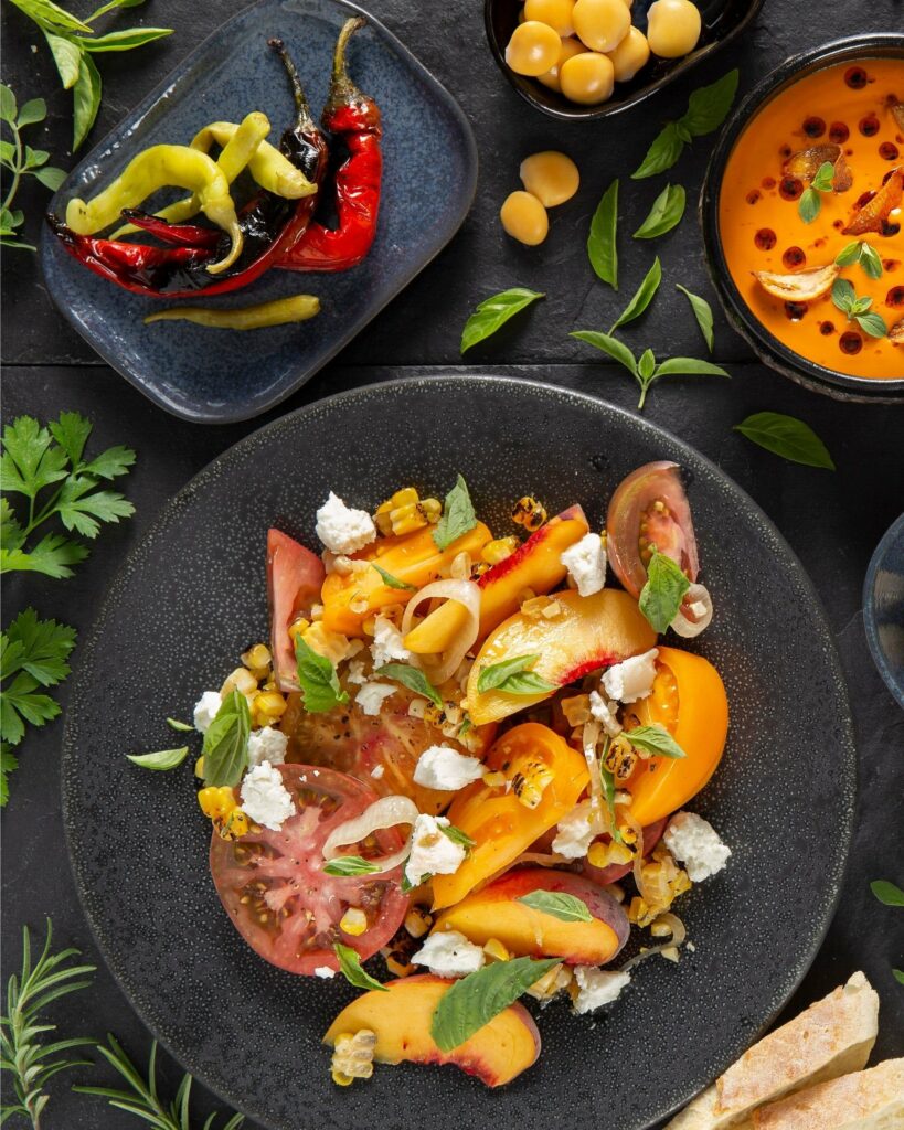 a colorful Tomato Peach Salad sits on a black plate
