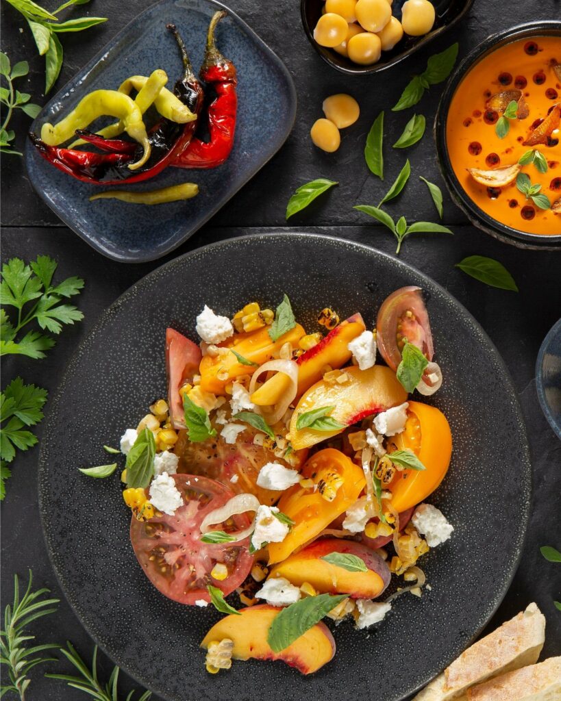 A colorful Tomato Peach Salad sits on a black plate