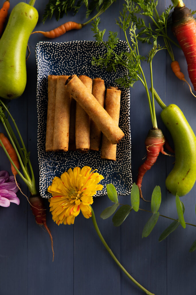 A New Year's Eve Hors D'oeuvres platter featuring a flat-lay image of a plate of spring rolls surrounded by colorful vegetables.