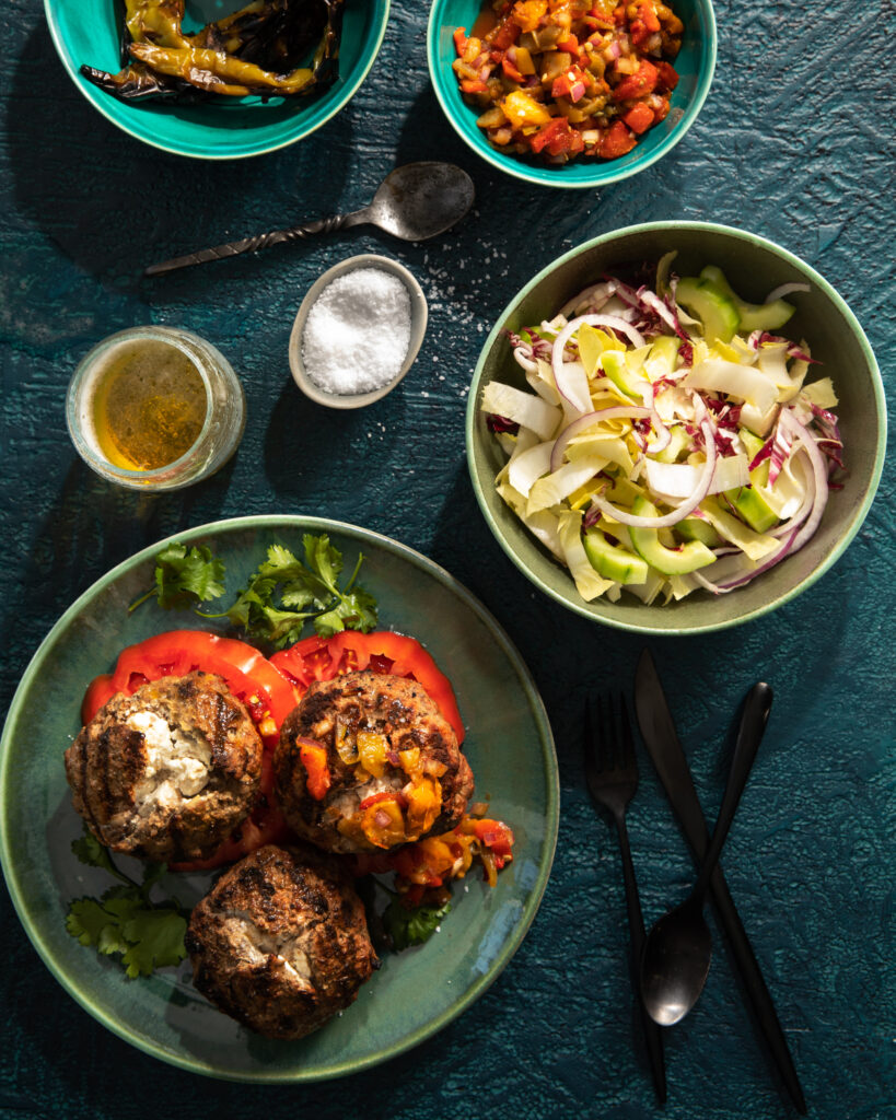 An aerial shot of Three Balkan Burgers sitting on a green plate. Off to the right side are bowls of toppings.