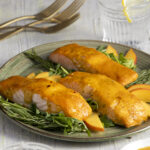 Three portions of salmon with a peach and yellow tomato sauce on a green plate with a white background.