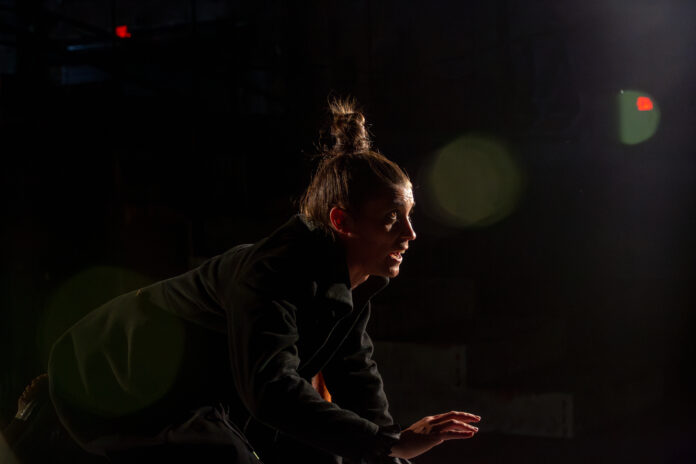 The side profile of a man with a top bun against a black background. They star as Hamlet in Quantum Theater's production of the play.