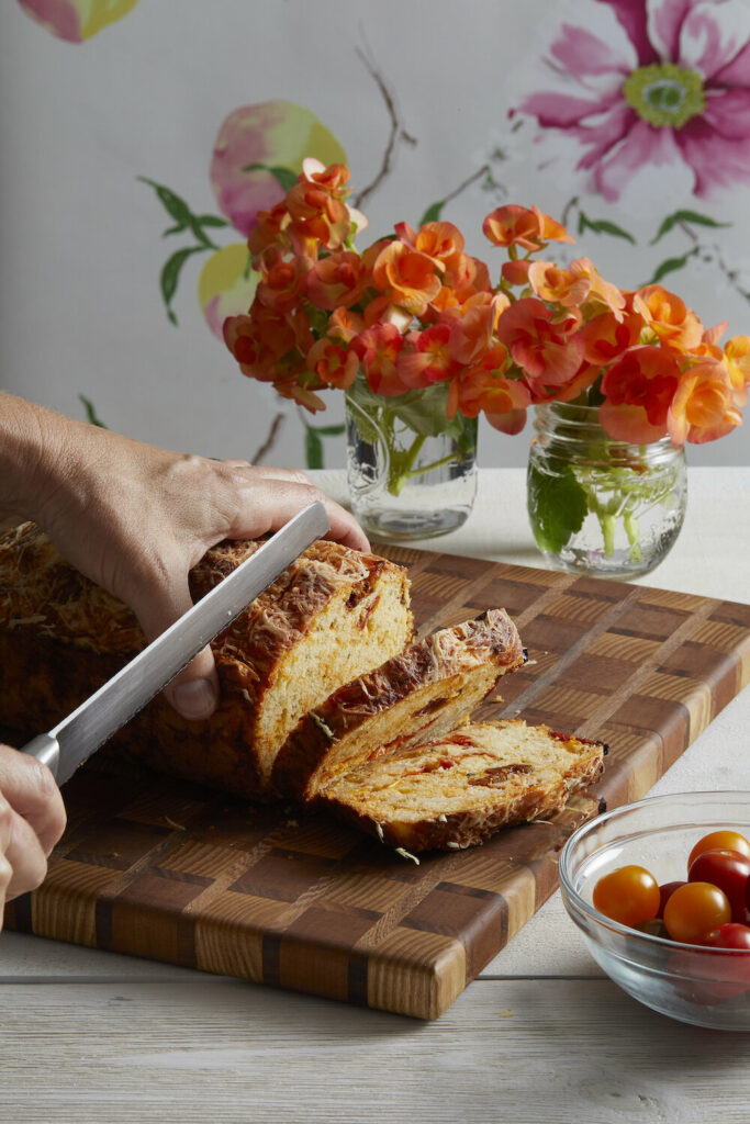 Roasted Cherry Tomato Cheese Bread placed on a brownish cake board being cut with a knife