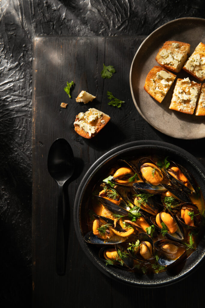 Sopa de Mariscos sits in a black bowl with high edges next to a plate of sourdough bread.