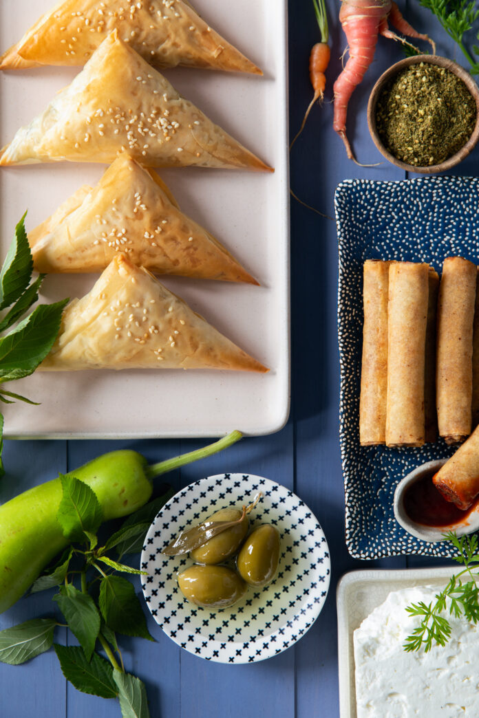 A flat-lay image of spinach pies and spring roll appetizers .