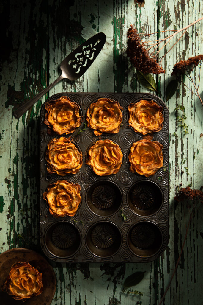 Flat-lay image of a muffin tin filled with sweet potato rosettes on a weathered table.