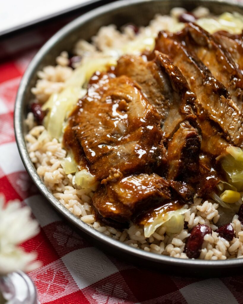 Jamaican Jerk Pork sits on a bed of rice in a silver bowl.