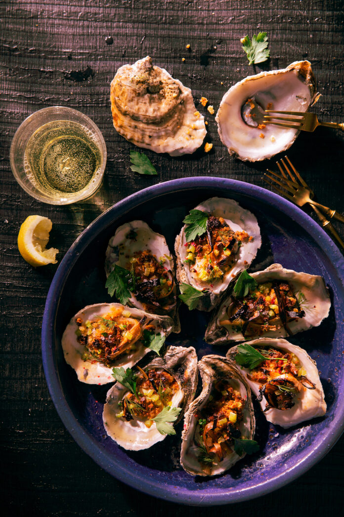 The Speckled Egg TABLE Magazine Roasted Oysters with Cornbread, Leek & Banana Pepper Crumble sit in a purple dish with high sides.