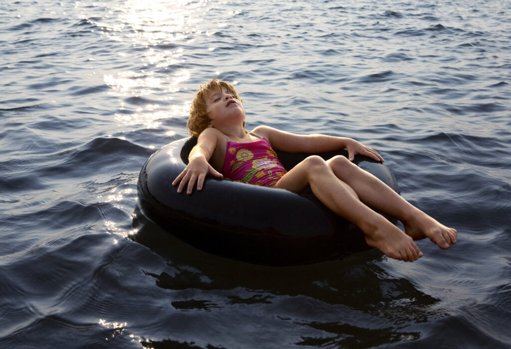 a young girl in a red one piece swimsuit lays in a black inflatable in dark blue water