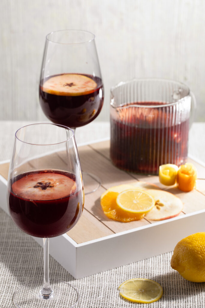 Two deep red sangria cocktails sit in wine glasses and garnished with lemon wedges. Sangria Recipe