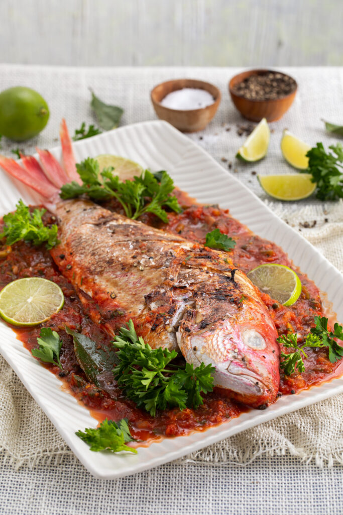 Red Snapper in Spicy Tomato Sauce sits on a white rectangle plate. Huachinango a la Veracruzana Recipe