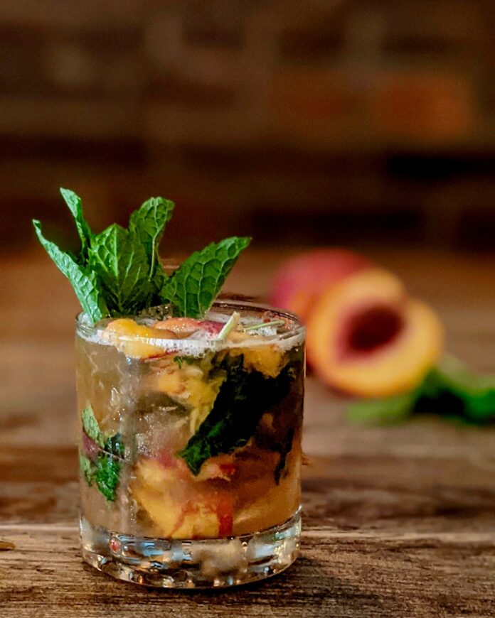 A cocktail dark orange in color sits in a rocks glass garnished with mint.