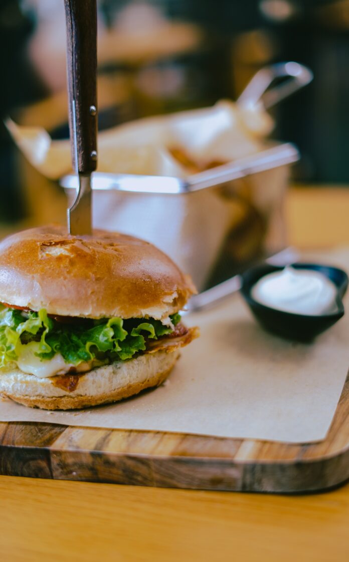 A burger with a knife sticking out of it sits on a wooden serving board. Great Pittsburgh Bar Food