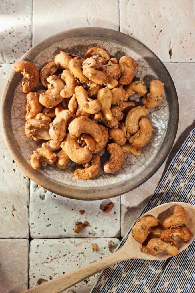 An aerial shot of herb roasted cashews on a white plate with brown trim. A spoon full of cashews sits off to the right.