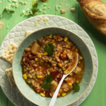 very simple, healthy, and nutritious Alphabet Soup in a light green bowl. on the right sit sits a loaf of crusty bread and saltines. Alphabet Soup Recipe