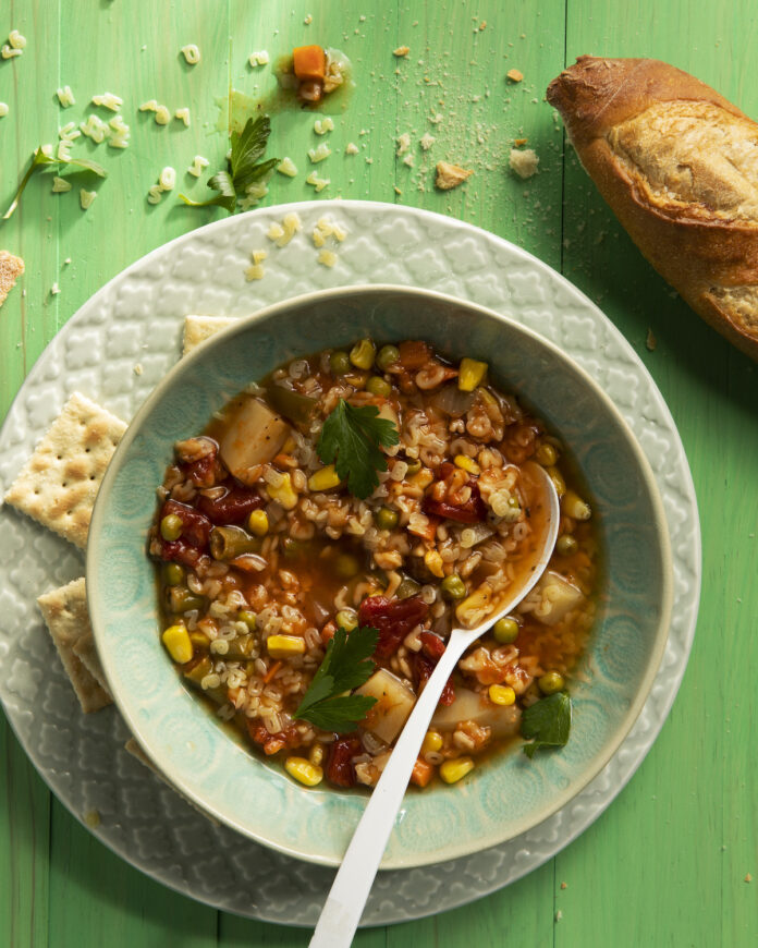 very simple, healthy, and nutritious Alphabet Soup in a light green bowl. on the right sit sits a loaf of crusty bread and saltines. Alphabet Soup Recipe
