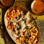 Rabbit Confit with Chanterelle Mushrooms and Eggplant Compote on an orange plate with two dishes of sauces at the top of the plate