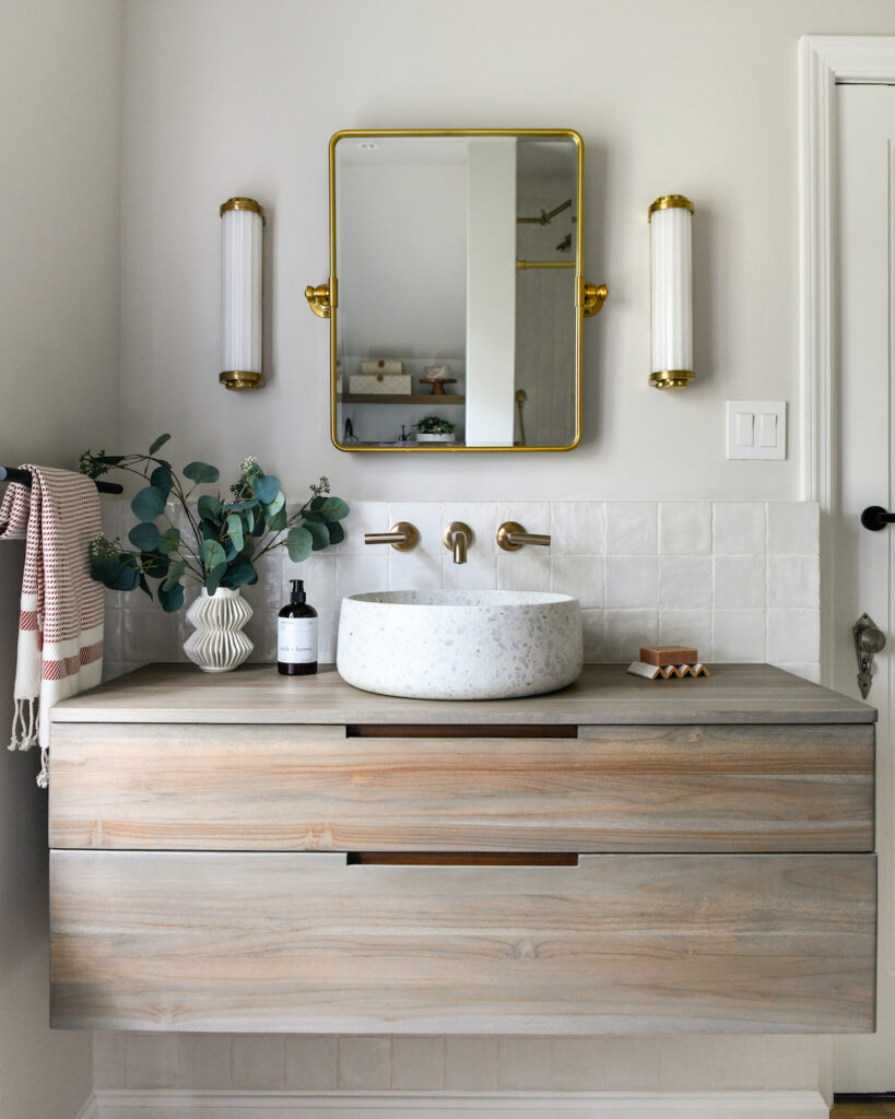 Amanda Boch's Bathroom Redesign. A marble bowl sink on a wooden vanity with a square mirror outline in gold