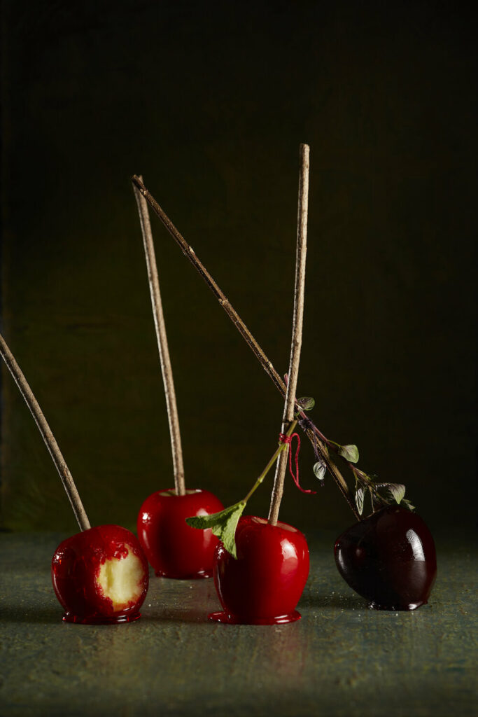 Red, candied apples sitting on a dark table, one apple has a bite taken out of it