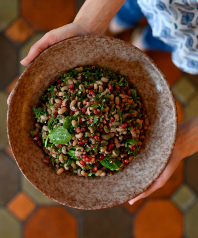 A pair of hands holds a black eyed pea salad, as part of a Sephardic Rosh Hashanah Menu