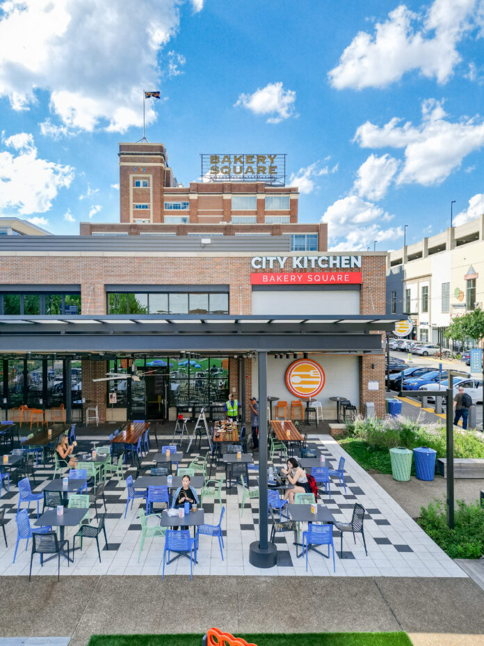 the exterior of City Kitchen Pittsburgh. the front of a building with bright blue skies in the background. many blue chairs sit out front