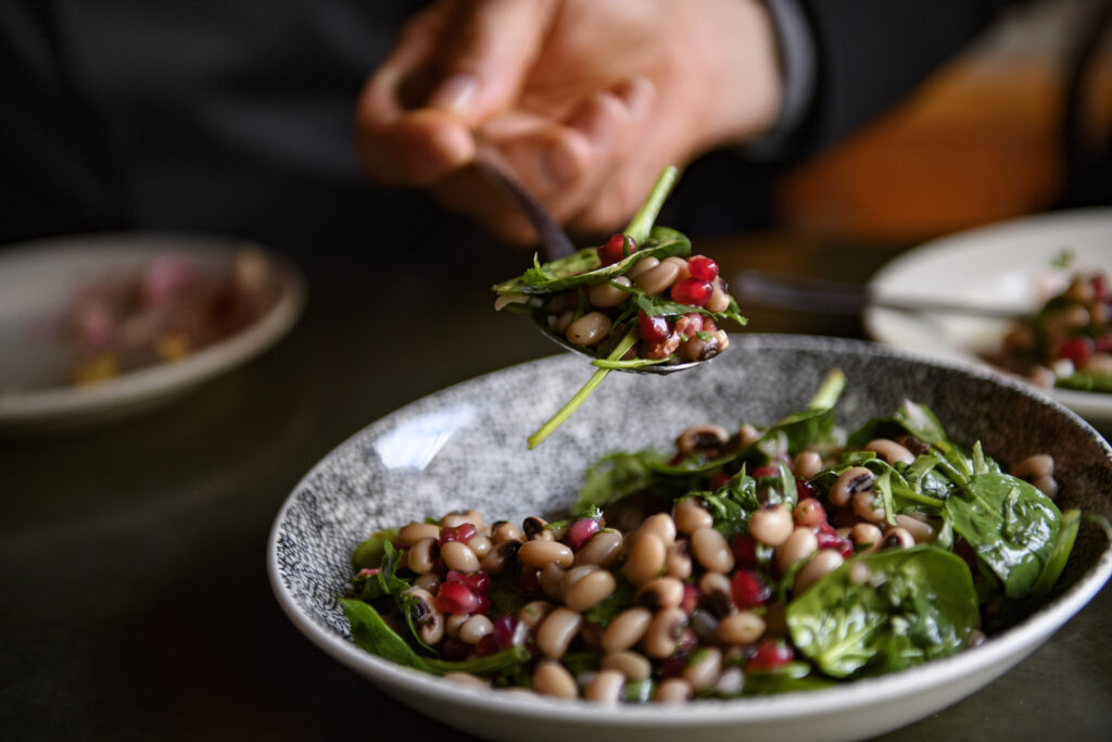 A white hand holding a spoonful of Black-Eyed Pea salad