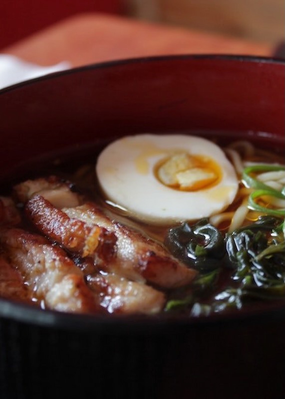 A bowl of hangover ramen with slices of pork, a soft boiled egg, and greens.