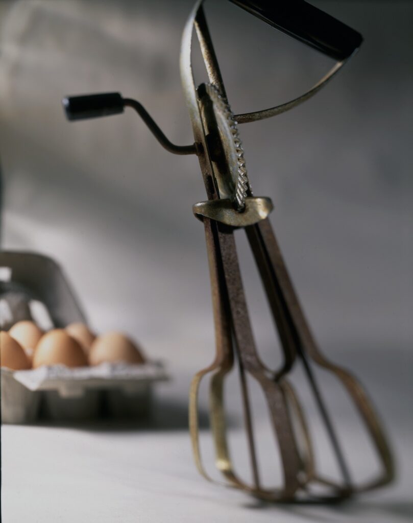 A pastry tool stands vertically in front of a carton of eggs