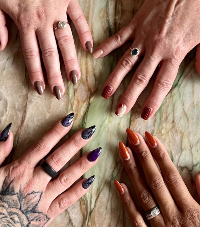 four women's hands are laid flat out on a slab of marble with various fall 2023 nail colors