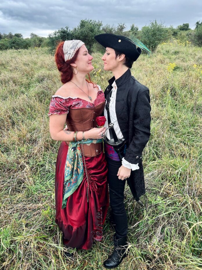 two women at the Pittsburgh Renaissance Festival. they stand in glass and face each other smiling