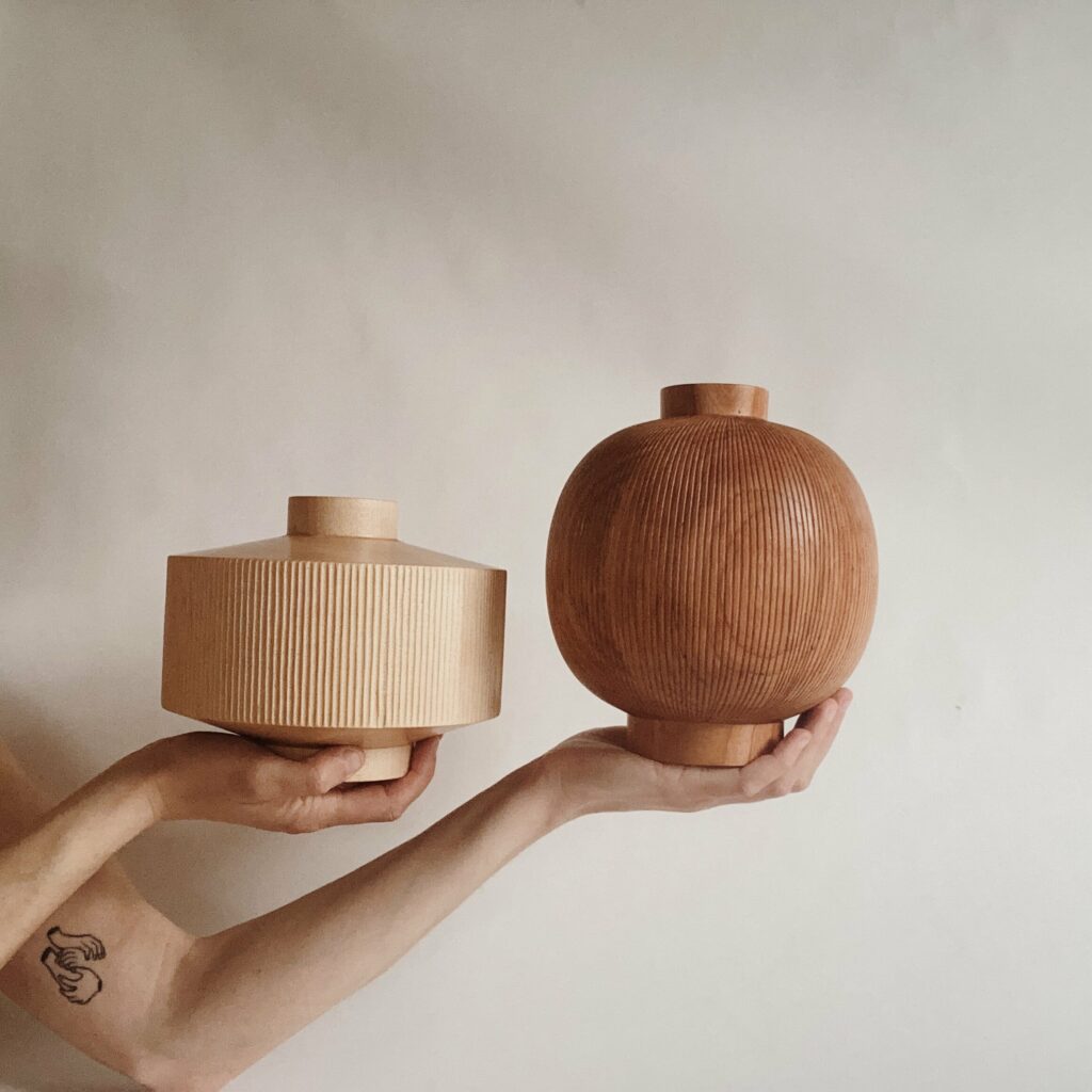 Two white hands hold wooden vases