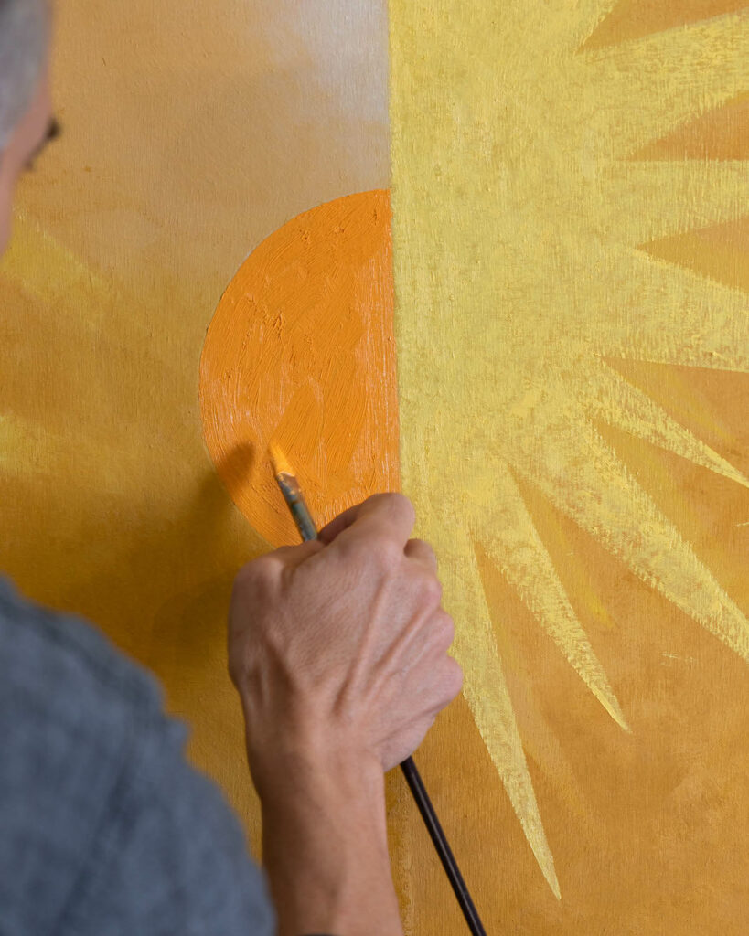 a hand paints a yellow sun