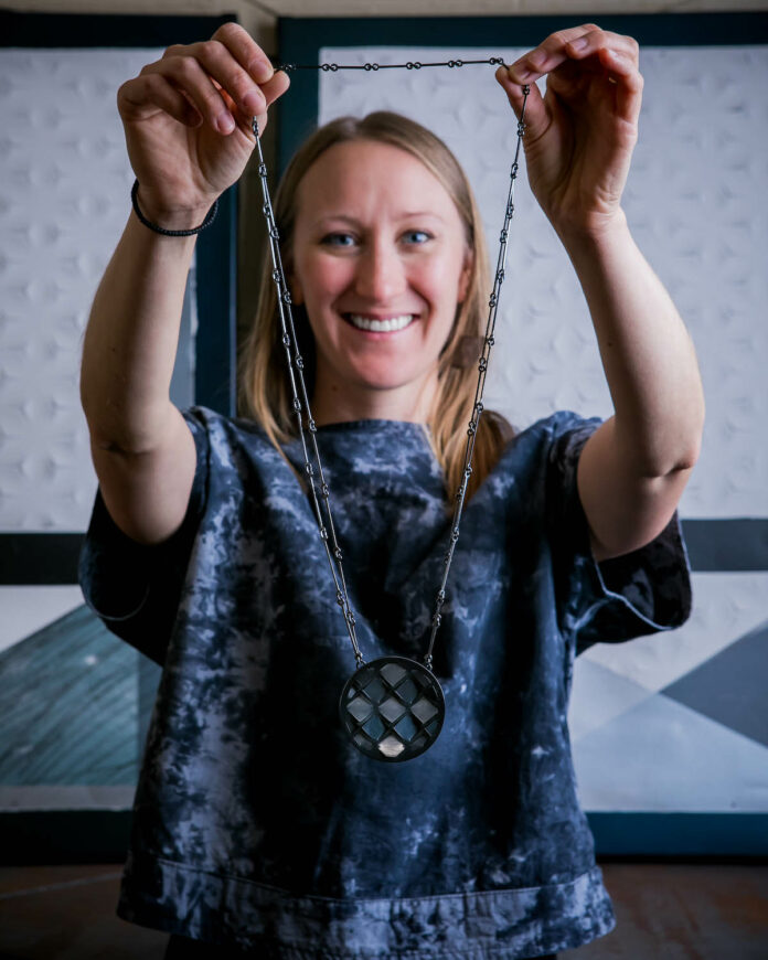 Metalsmith and sculptor Katie Rearick holds up a metal necklace in front of her and smiles