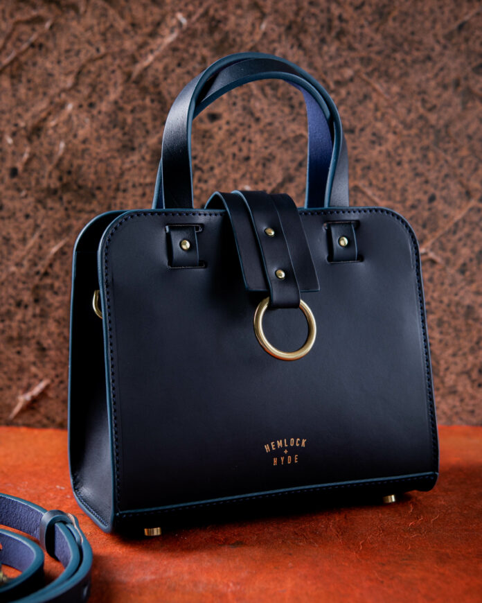 A black handmade leather handbag with gold details, stamped Hemlock and Hyde on the bottom front of the bag