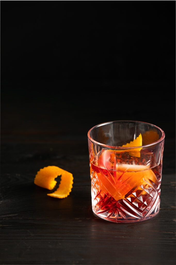 A light red cocktail in a rocks glass with an orange peel inside the glass. Negroni Con Alma Recipe