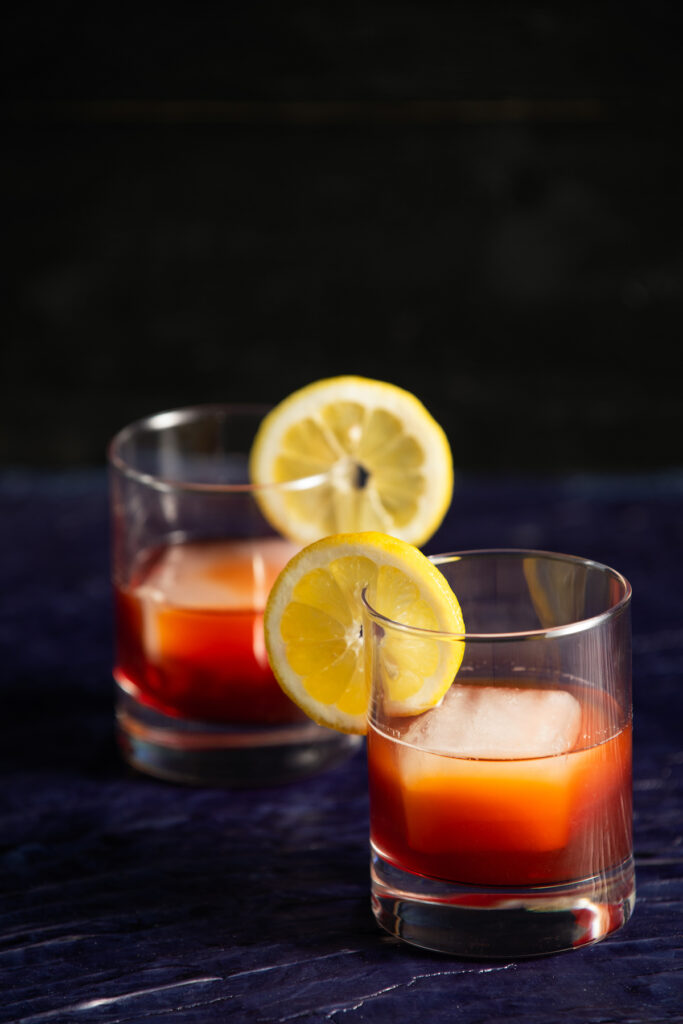 An two Earl Grey Negronis sits in round cocktail glasses, garnished with a lemon wedge.