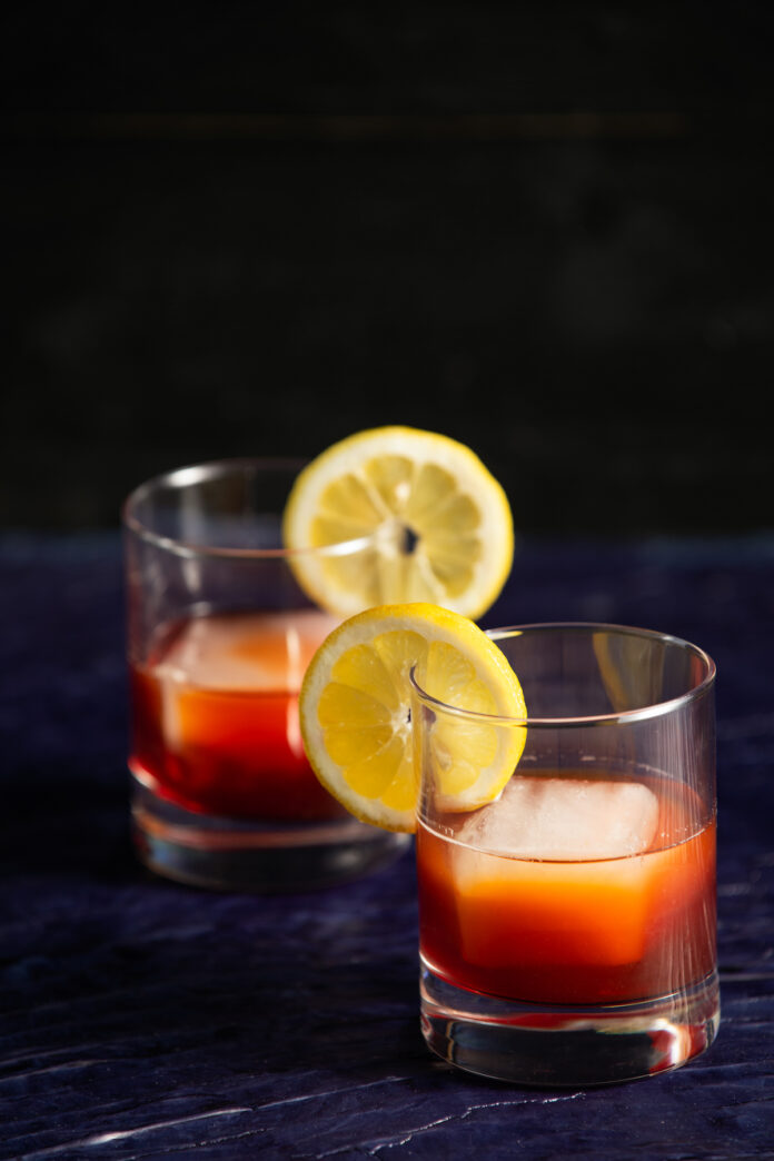 Earl Grey Negroni Cocktail Recipe An two Earl Grey Negronis sits in round cocktail glasses, garnished with a lemon wedge.