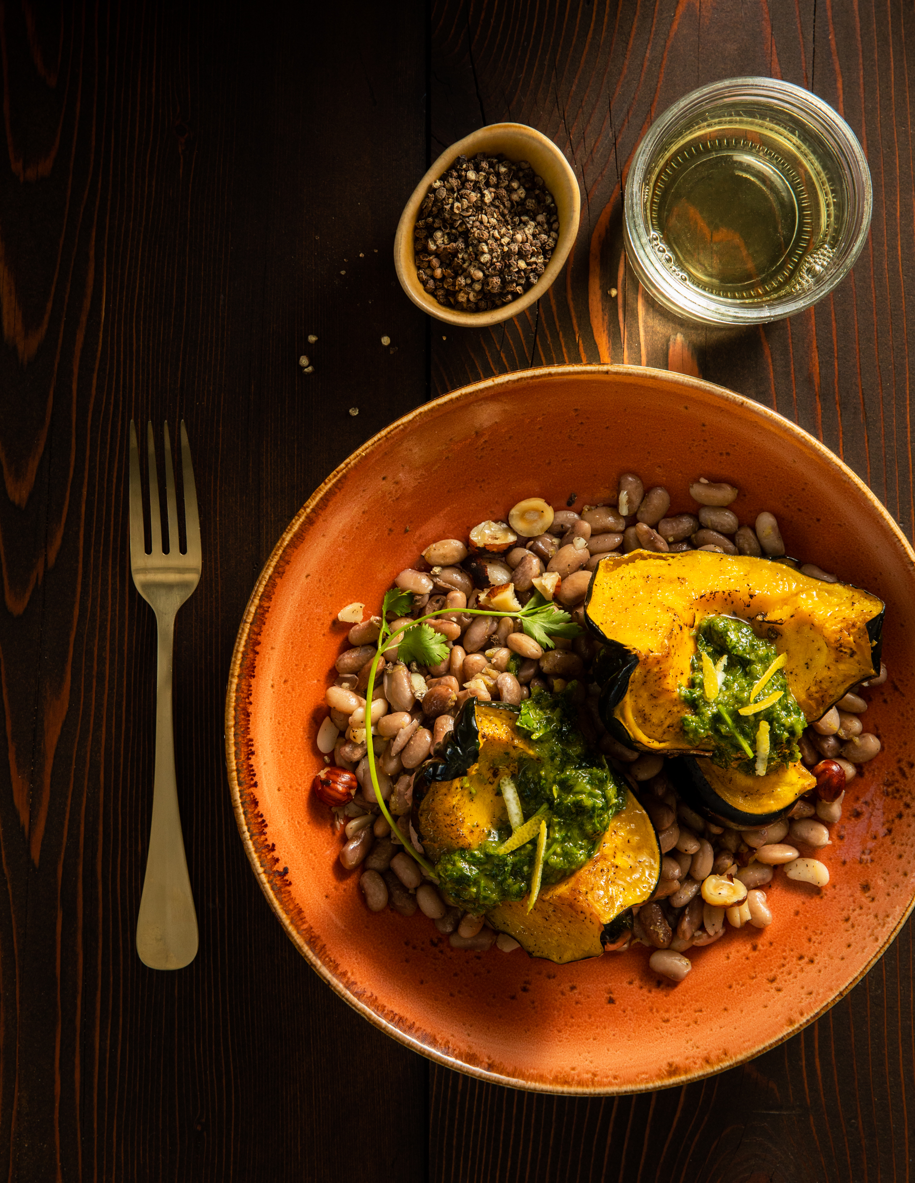 A side dish of Roasted Acorn Squash with Lemony Pinto Beans and Zhoug in an orange bowl. A gold spoon sits to the left. Zhoug Recipe