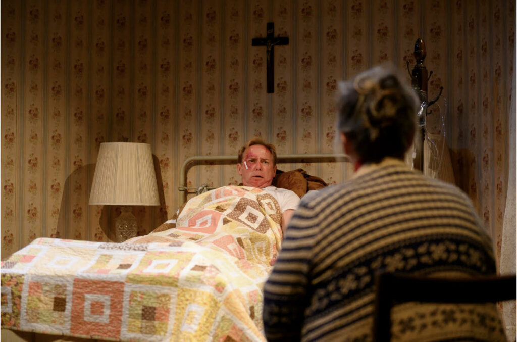 From barebones productions' 2023 performance of Stephen King's Misery a man sits in a bed with a quilt