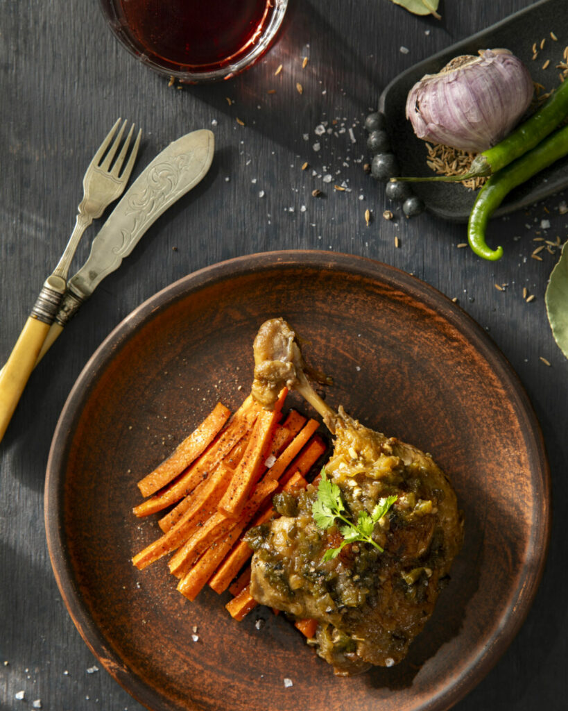 Plated braised duck leg in green chiles and roasted cumin carrot strips topped with parsley.