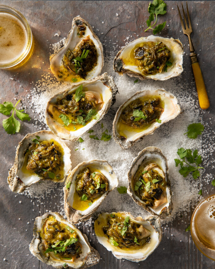 Grilled oysters displayed with a cilantro topping on a wooden table.