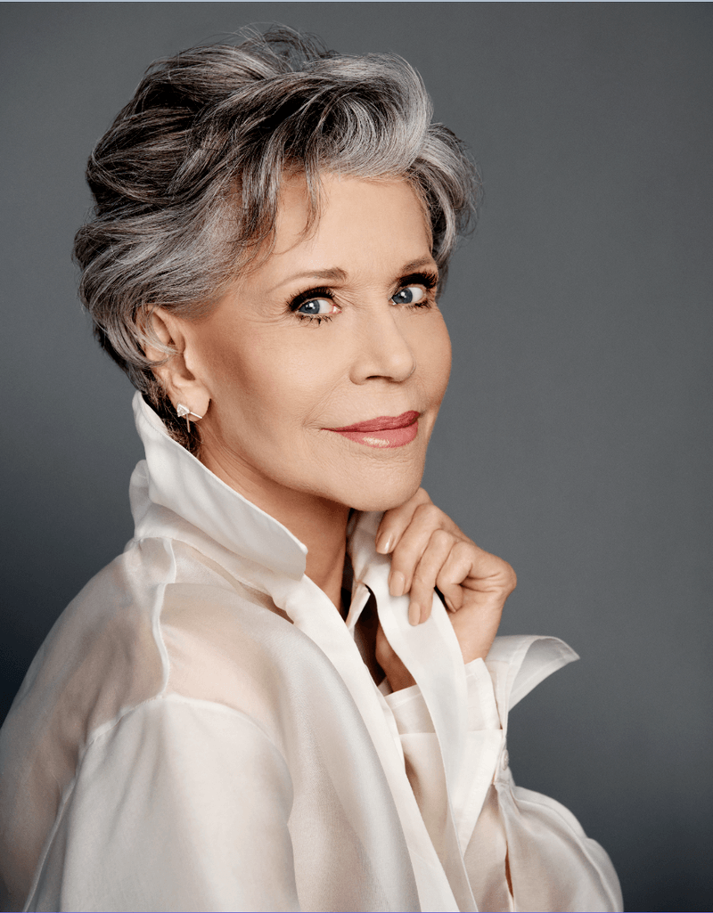 jane fonda poses with a short grey haircut. she looks to the camera with her left hand on her chin