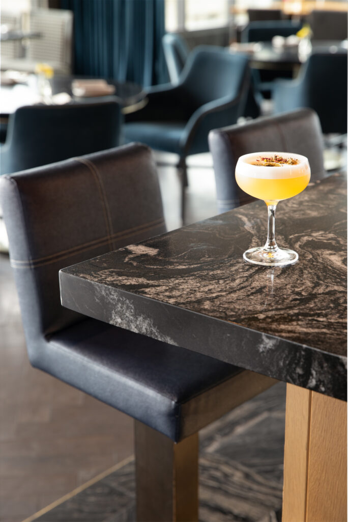 A cocktail yellow in color, sits in a martini glass on a black marble table. chamomile tea cocktail
