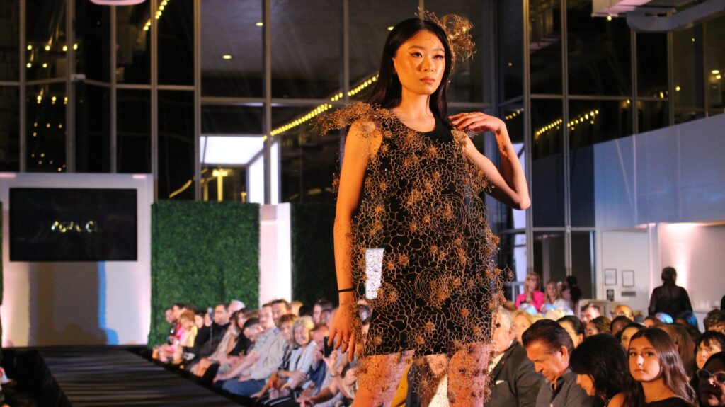 A woman in a short sparkly dress poses at the end of a runway