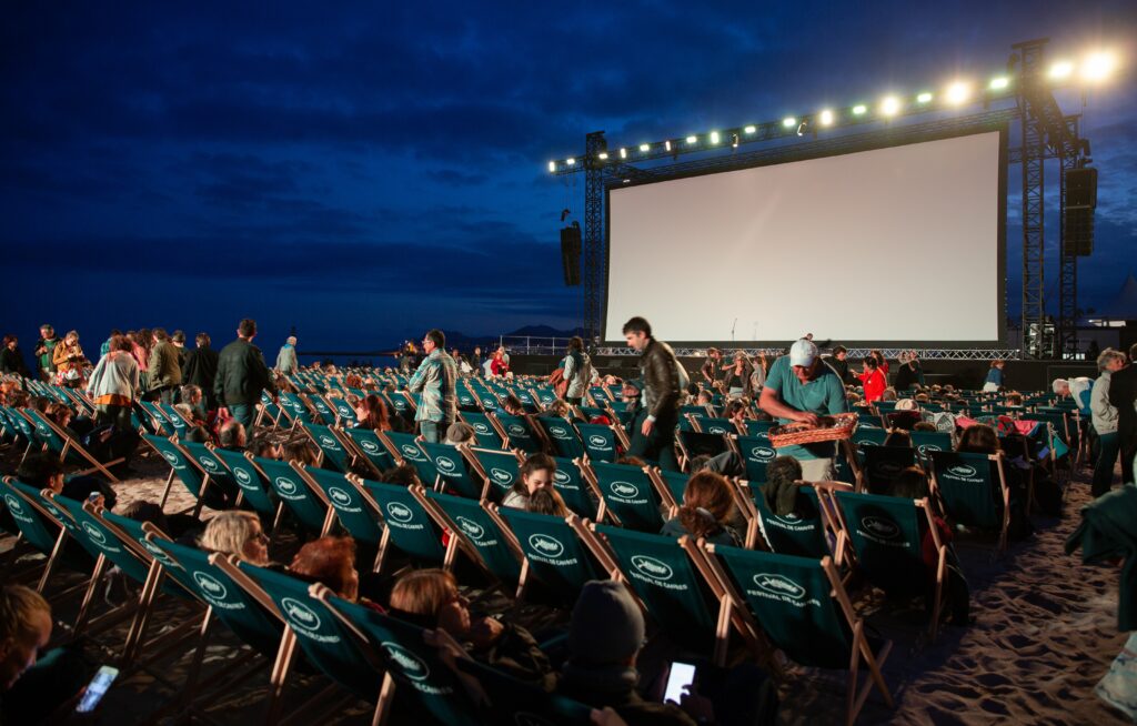 An outdoor movie setup with rows of folding chairs in front of a pull down screen