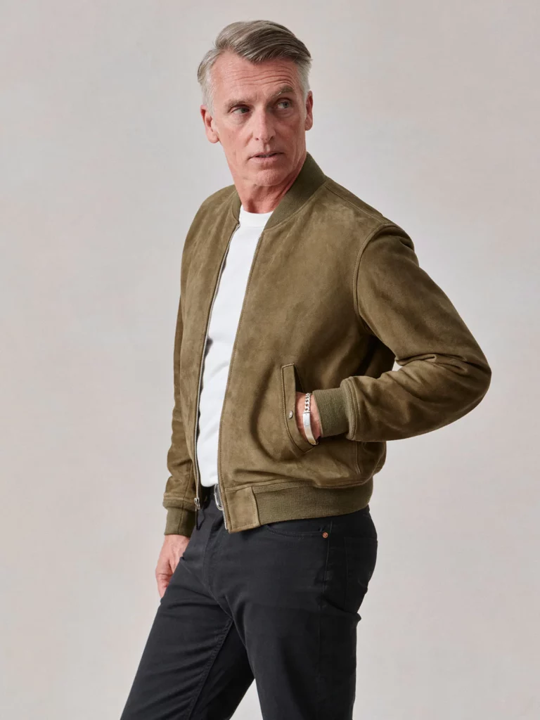 A grey-haired man modeling in a tan bomber jacket.